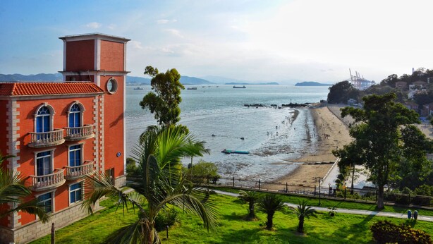 A coastal building with a red facade, a balcony, and a view of the beach and sea. - Marine Garden Hotel (Xiamen)
