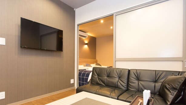 A modern hotel room with a flat-screen TV mounted on the wall, a leather sofa, and a wooden coffee table. - Group STAY CLASSE 02 (Osaka)