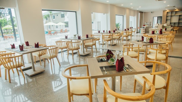 A spacious dining area with multiple tables and chairs, large windows offering views of the outdoor pool area. - Green Hotel Danang (Da Nang)
