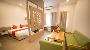 A modern hotel room with a bed, a green sofa, a wooden table, and a partition with a lattice design. - Green Hotel Danang (Da Nang)