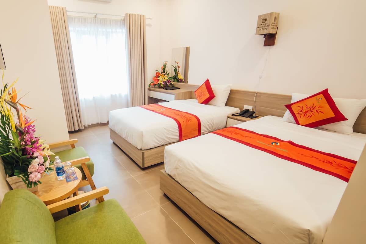 A hotel room with two beds, a desk, a chair, and a window with curtains.