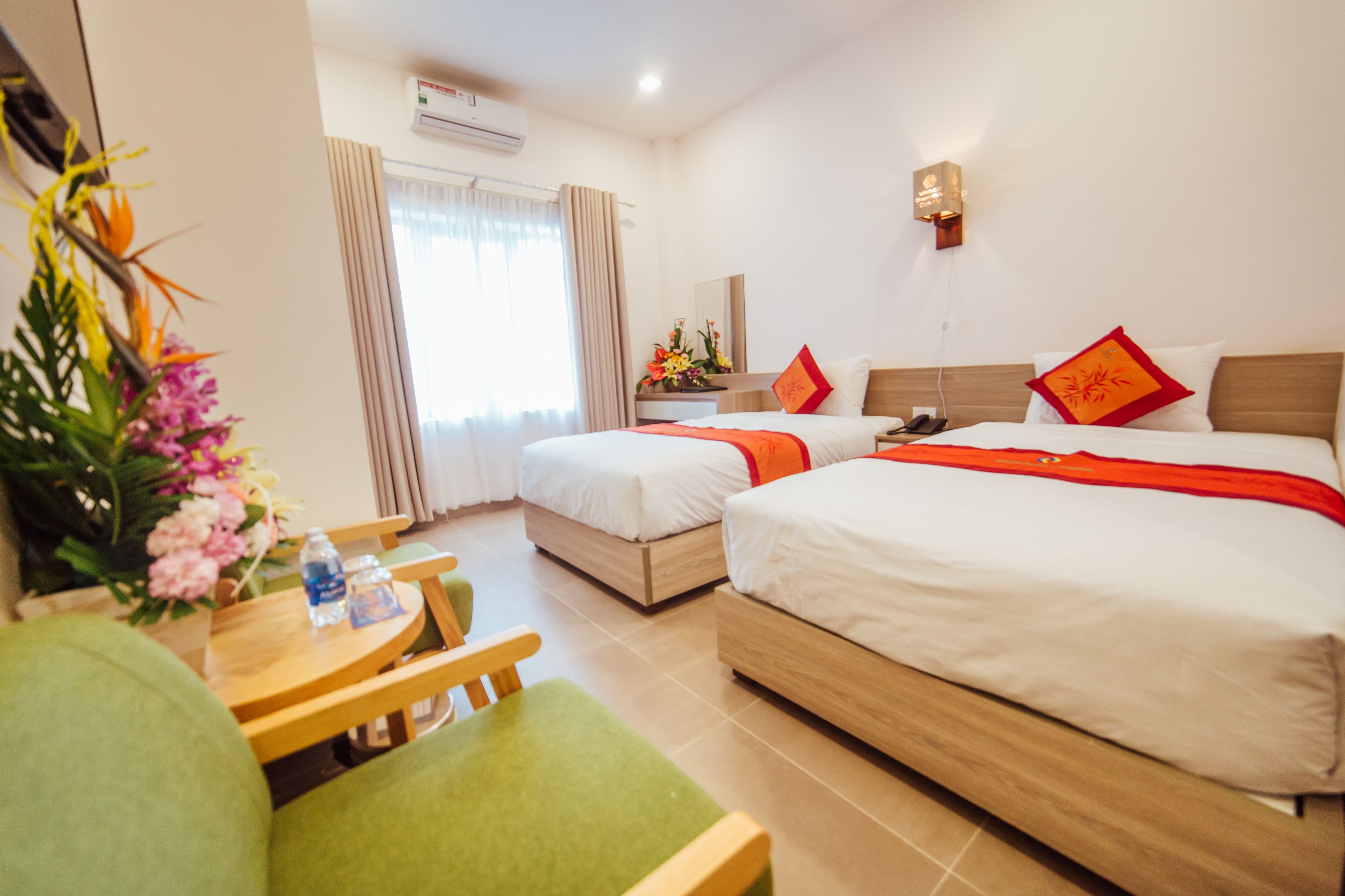 A hotel room with two beds, a desk with a chair, and a small table with a vase of flowers.