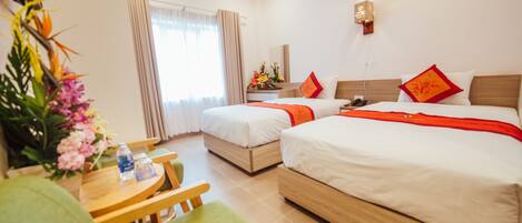 A hotel room with two beds, a desk with a chair, and a small table with a vase of flowers.