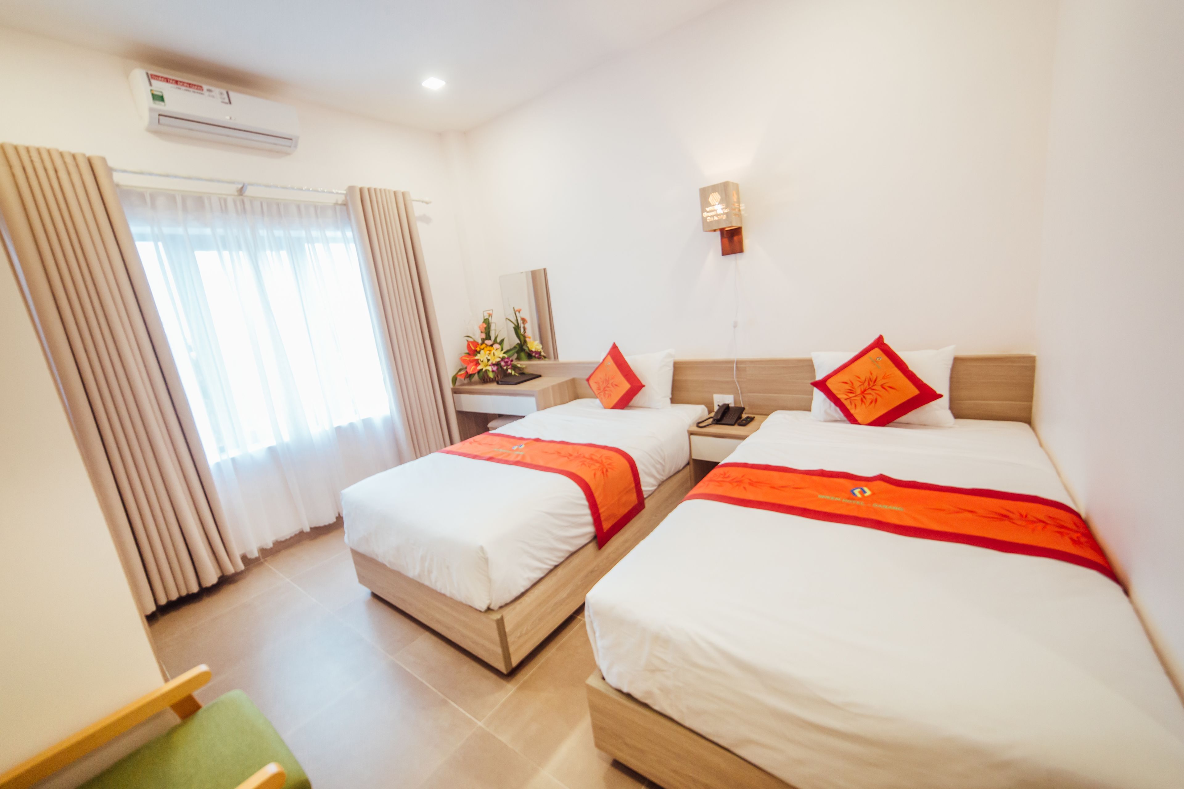 A hotel room with two beds, a desk with a telephone, and a small table with a vase of flowers.