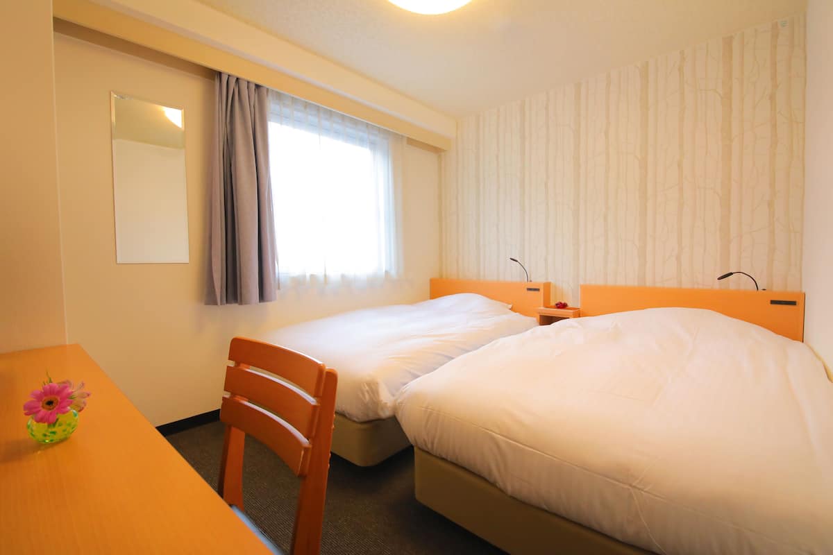 A hotel room with two beds, a desk, a chair, a mirror, and a window with curtains.