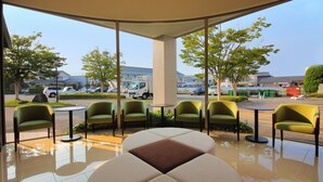 A modern outdoor seating area with green chairs and a central table, overlooking a parking lot and buildings. - Smile Hotel Anan (Anan)