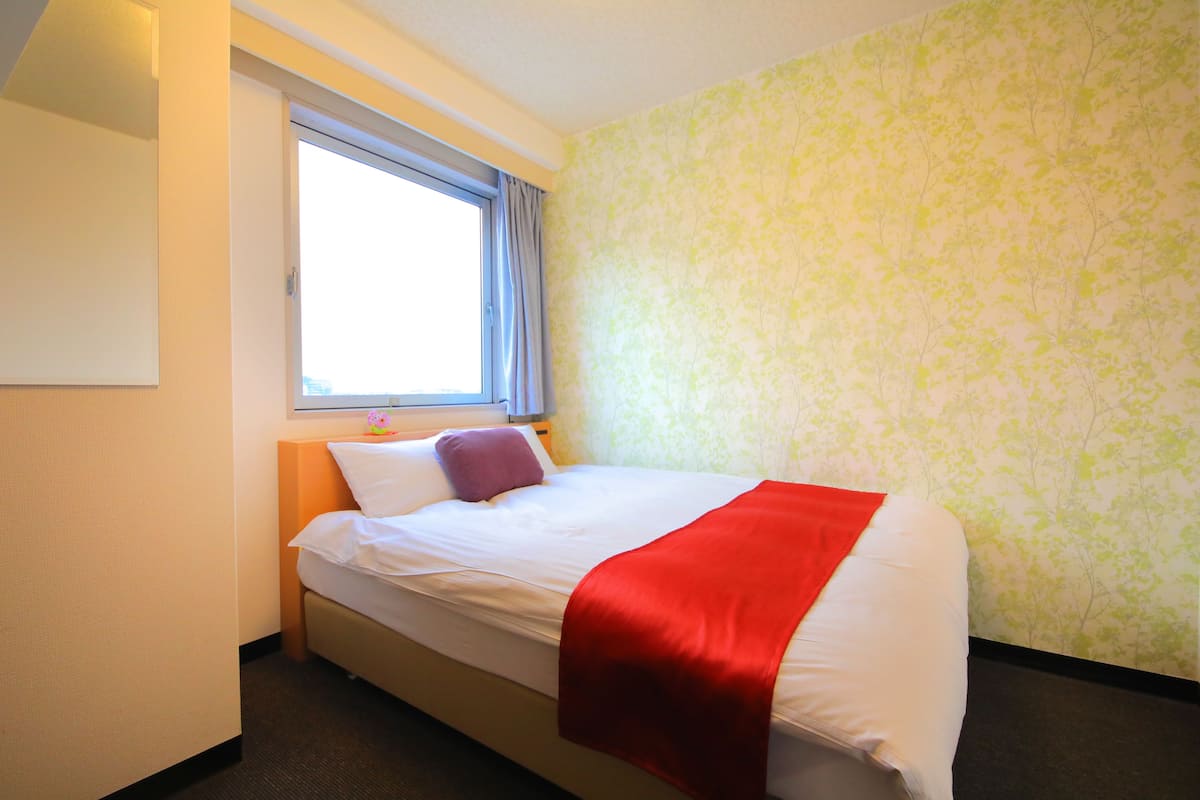 A hotel room with a bed, a window with curtains, and floral wallpaper.