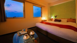 A hotel room with a bed, a bedside table with a book and two cups, a window with a view of the sky, and a green wall with a pattern. - Smile Hotel Anan (Anan)