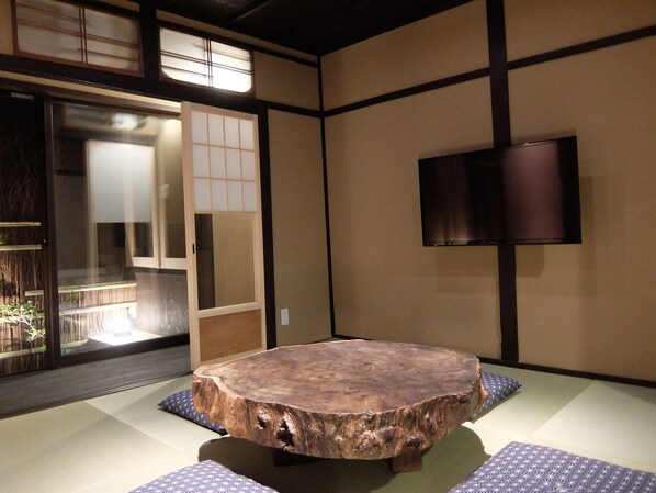 Una habitación japonesa tradicional con suelo de tatami, una mesa de madera, puertas correderas y un televisor montado.