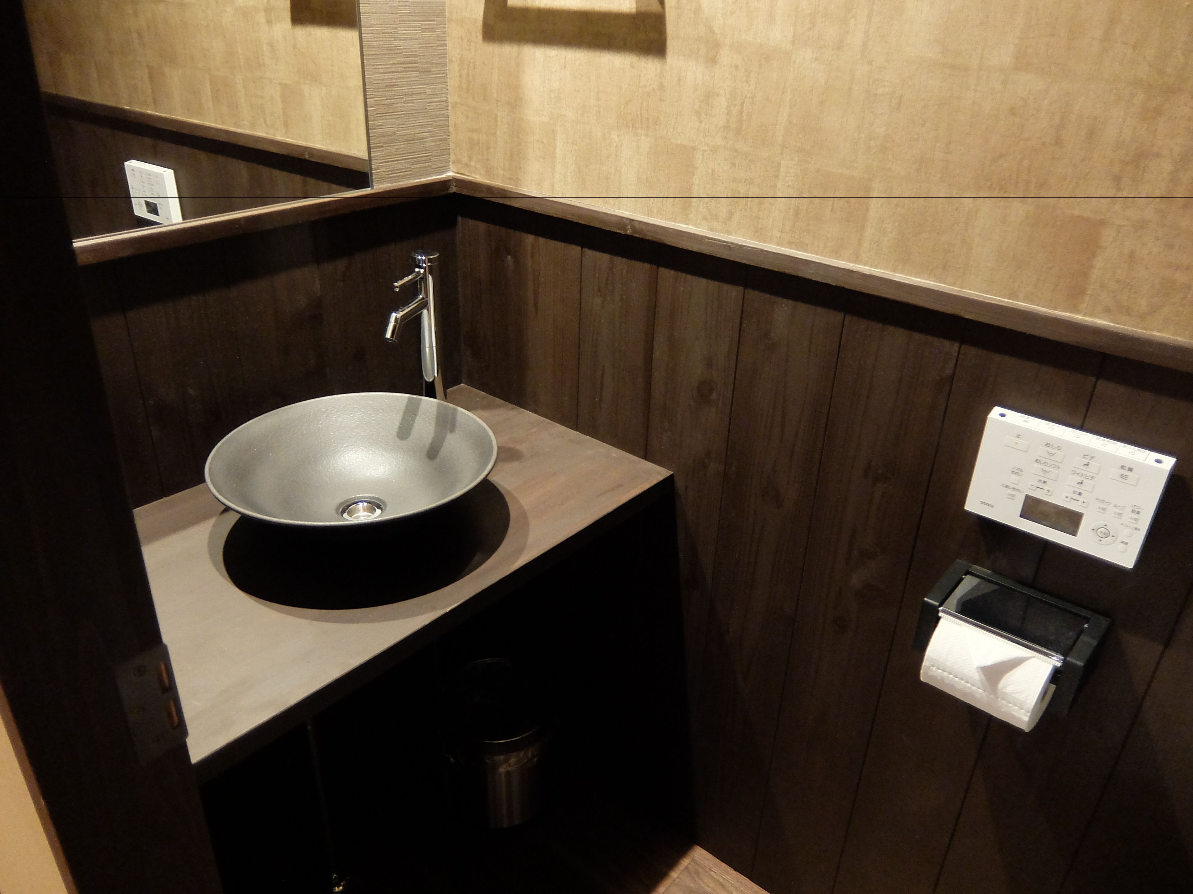 Une salle de bain moderne avec un lavabo rond, un miroir et un distributeur de papier toilette fixé au mur.