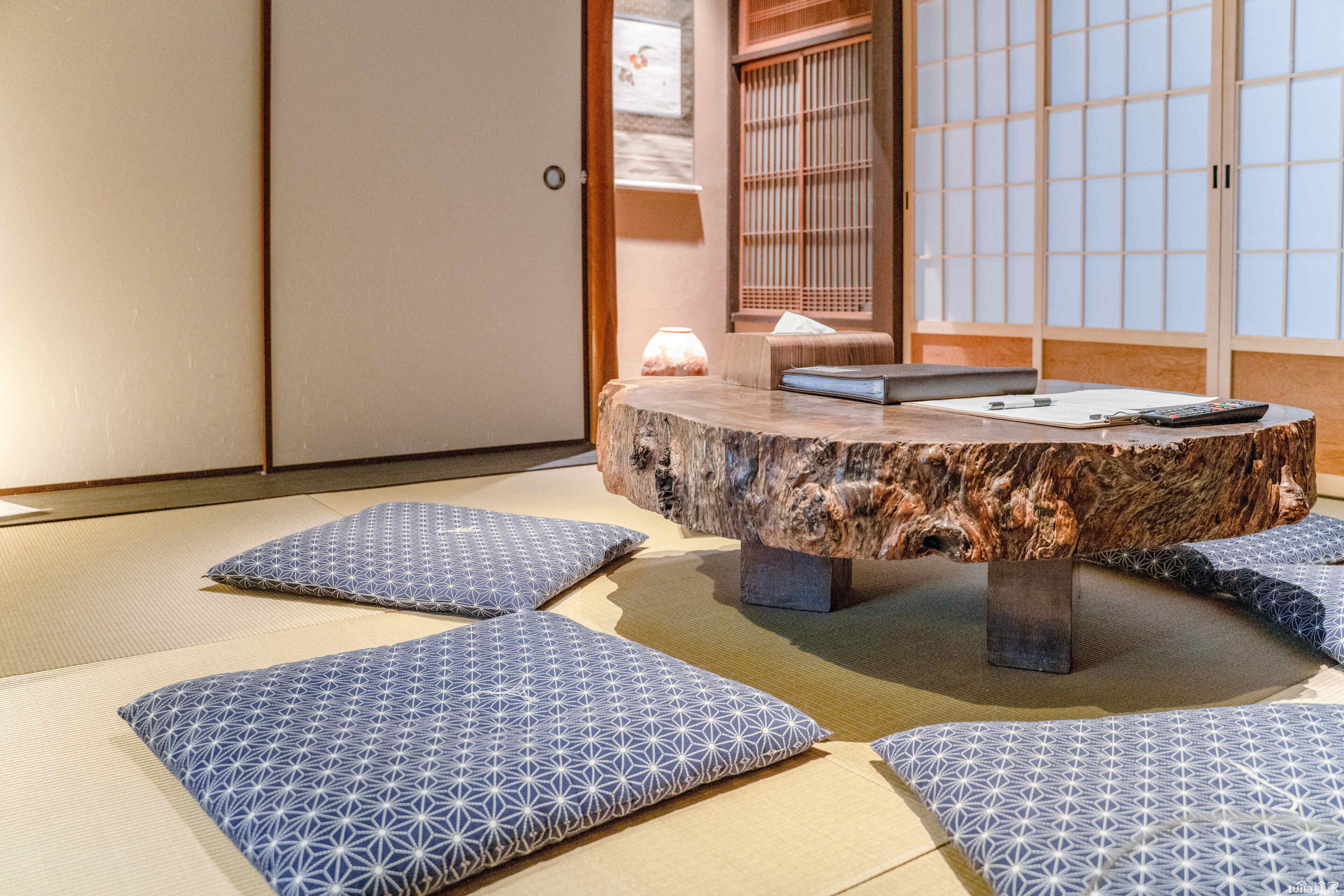 A tatami mat room with a central tatami mat table, cushions, a lamp, and sliding doors.