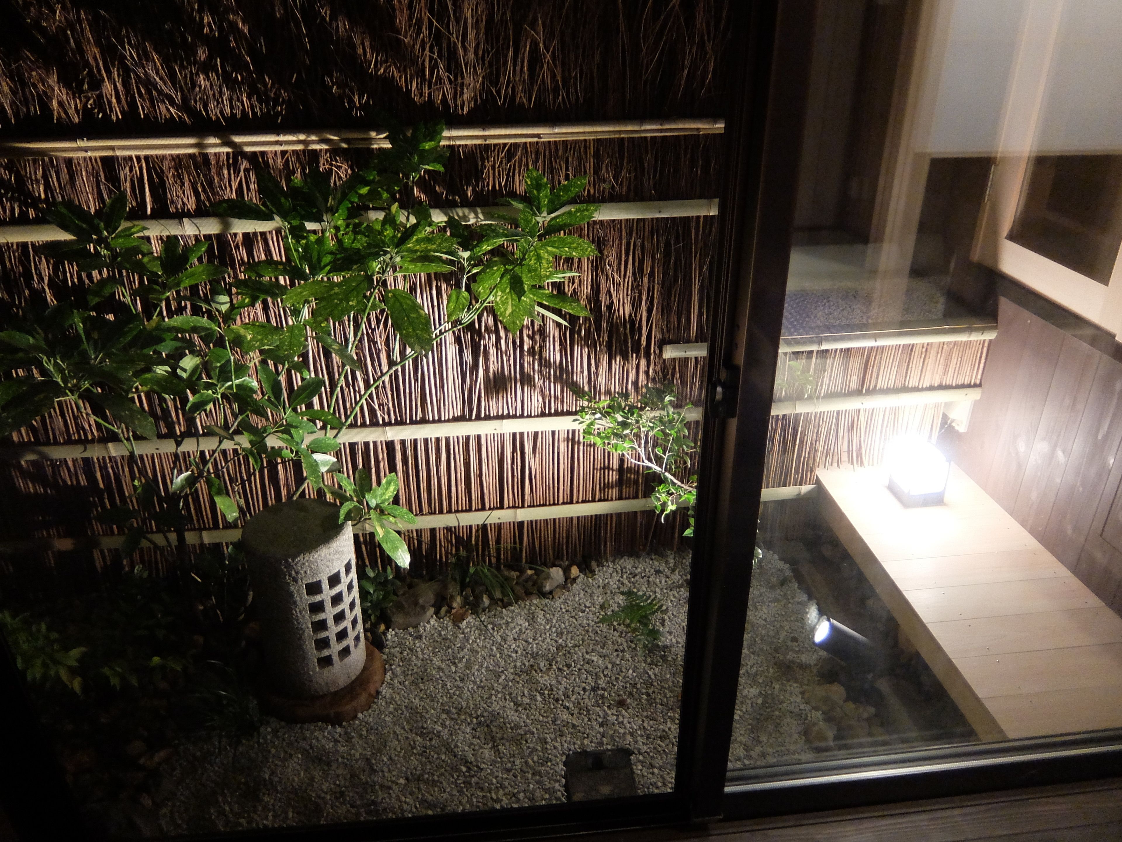 Une pièce avec une clôture en bambou, une plante en pot et une petite table avec une source de lumière.