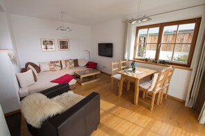 A living room with a sofa, a coffee table, a TV, and a dining table with chairs. - Ferienwohnung F9 (Garmisch-Partenkirchen)