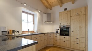 A modern kitchen with wooden cabinets, a built-in oven, and a large island with a black countertop. - Ferienwohnung F9 (Garmisch-Partenkirchen)