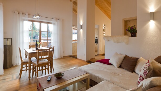 A spacious living area with a wooden dining table, a sofa, and a kitchen in the background. - Ferienwohnung F9 (Garmisch-Partenkirchen)