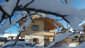 A wooden chalet with a balcony, surrounded by snow-covered trees. - Ferienwohnung F9 (Garmisch-Partenkirchen)