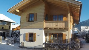 A two-story wooden chalet with a balcony, snow-covered surroundings, and a clear blue sky. - Ferienwohnung F9 (Garmisch-Partenkirchen)