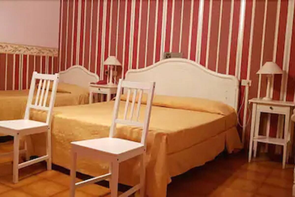 A hotel room with two single beds, a large bed, white chairs, and a striped wall.