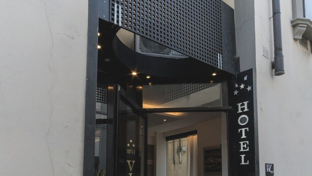 La entrada del Hotel Victoria, con estructura de metal negro y puertas de vidrio.