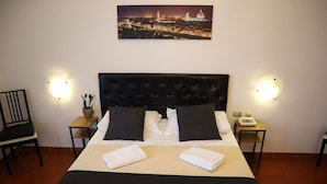 Habitación de hotel con una cama grande, dos mesitas de noche, una silla y un cuadro de un paisaje urbano en la pared.