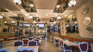 Un restaurante con varias zonas de comedor, incluyendo mesas y cabinas, con iluminación colgante y espejos decorativos en las paredes.