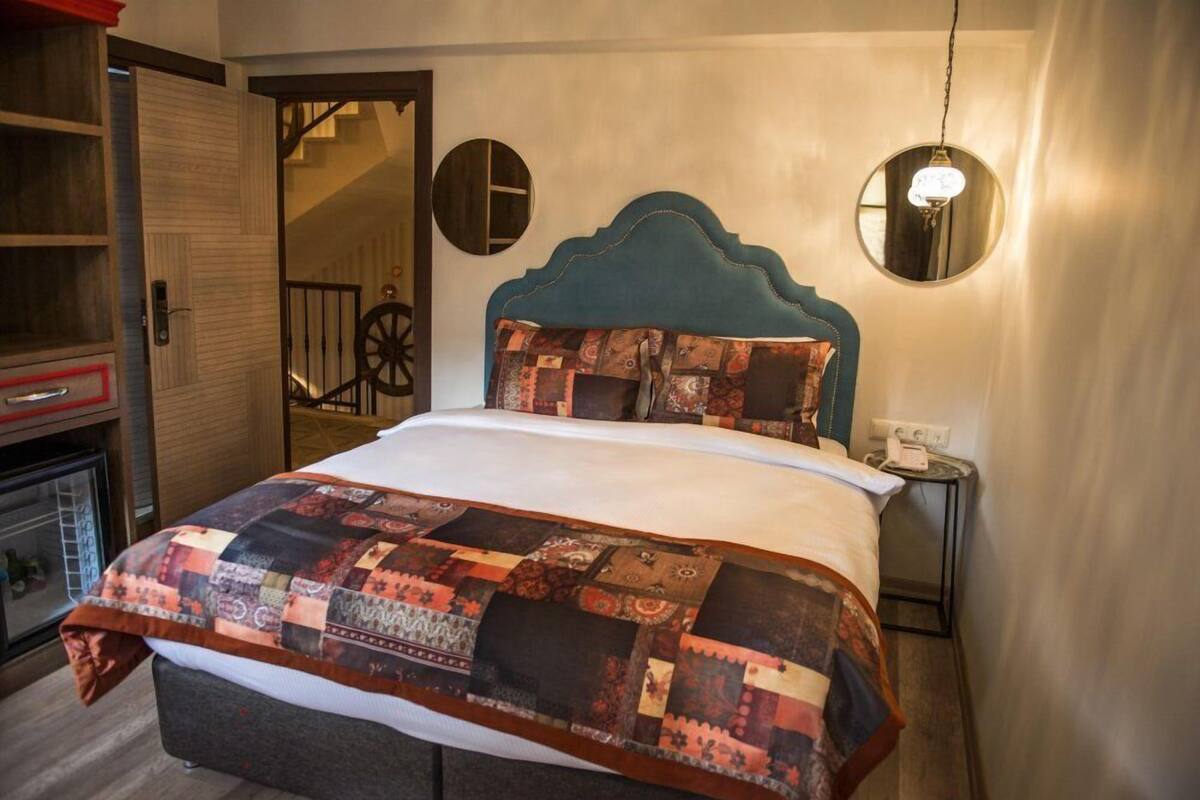 Una cama con colcha, un armario de madera, un espejo y una mesita de noche con lámpara.