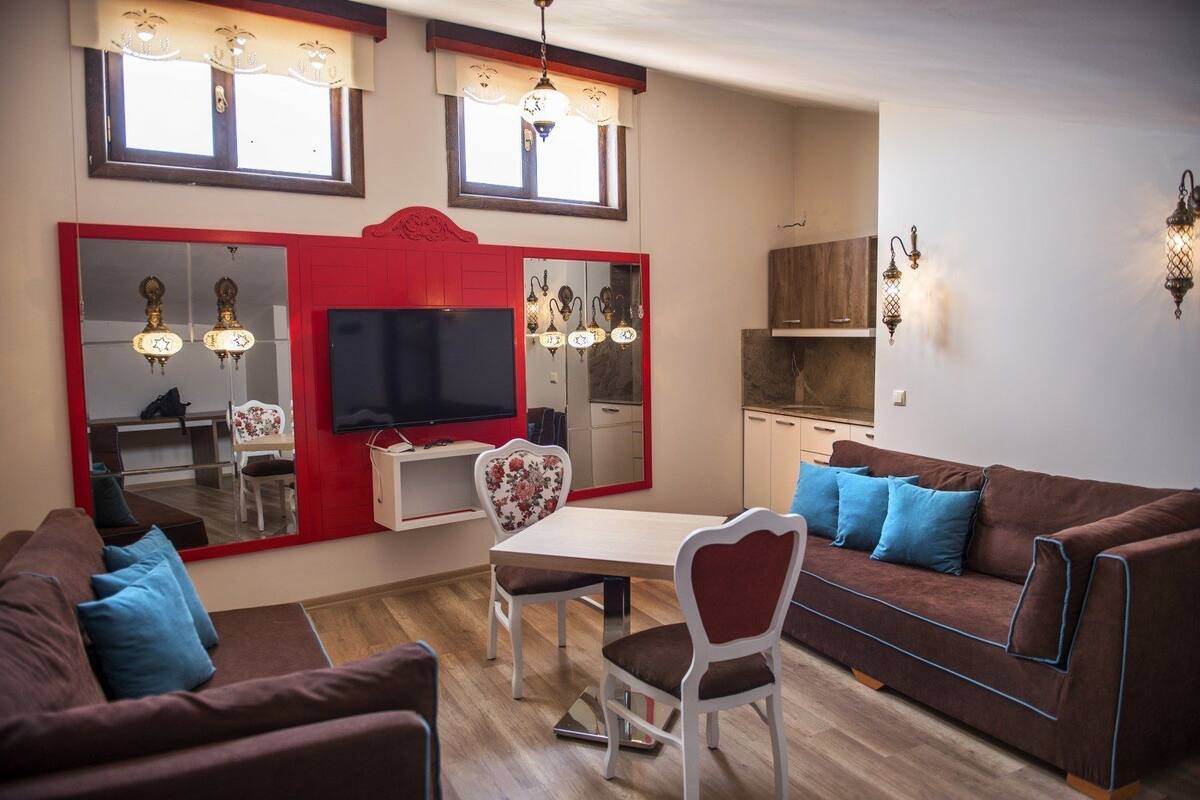 Una sala de estar con una pared de acento roja, un televisor, una mesa de comedor con sillas y un sofá marrón con cojines azules.