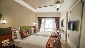 Una habitación de hotel con dos camas, un televisor, una mesita y una ventana con cortinas.