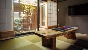 A traditional Japanese room with tatami flooring, a wooden table with books, sliding doors, and a television on the wall. - Reikaku Yasaka (Kyoto)