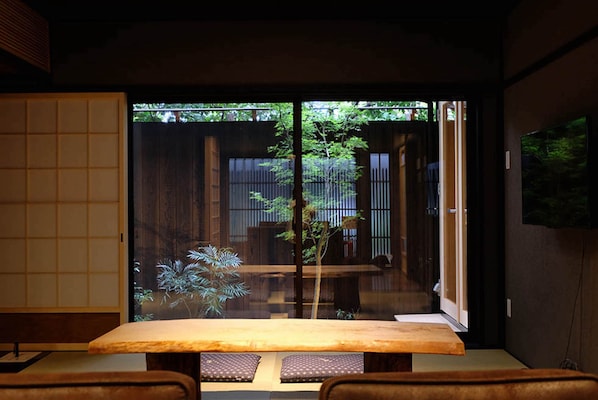 A traditional Japanese room with tatami flooring, a low table, and sliding doors leading to a garden.