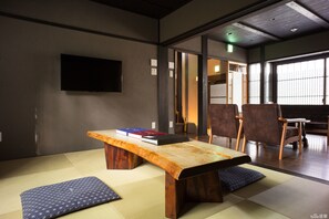 A traditional Japanese room with tatami flooring, a low wooden table, and a television mounted on the wall.