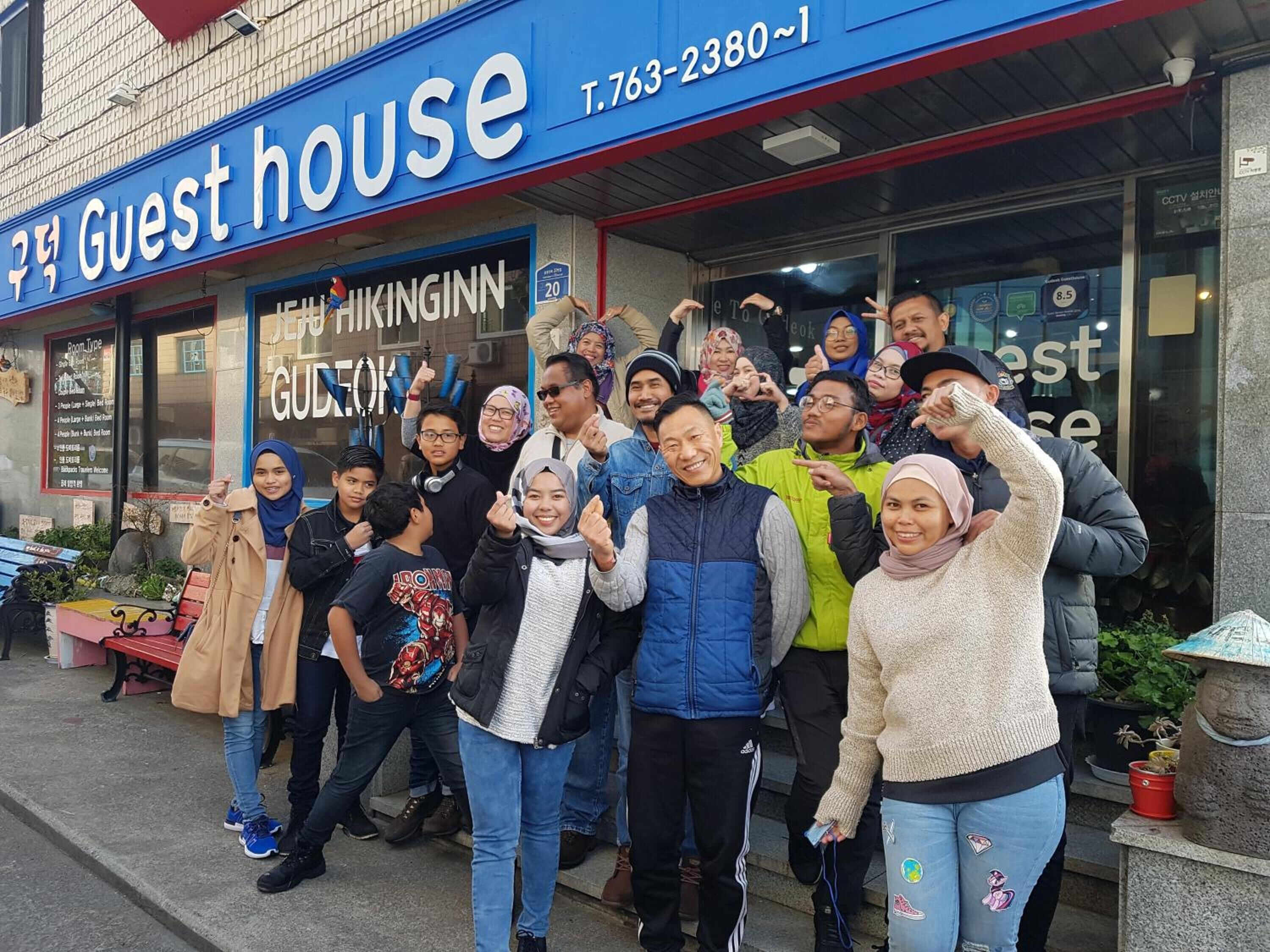 A group of people posing in front of a building with a sign reading "Guest house" and "HIKINGINN GUDEOK".