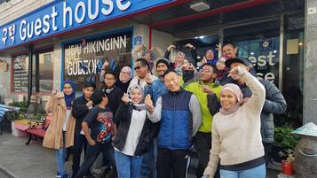 A group of people posing in front of a building with a sign reading "Guest house" and "HIKINGINN GUDEOK".