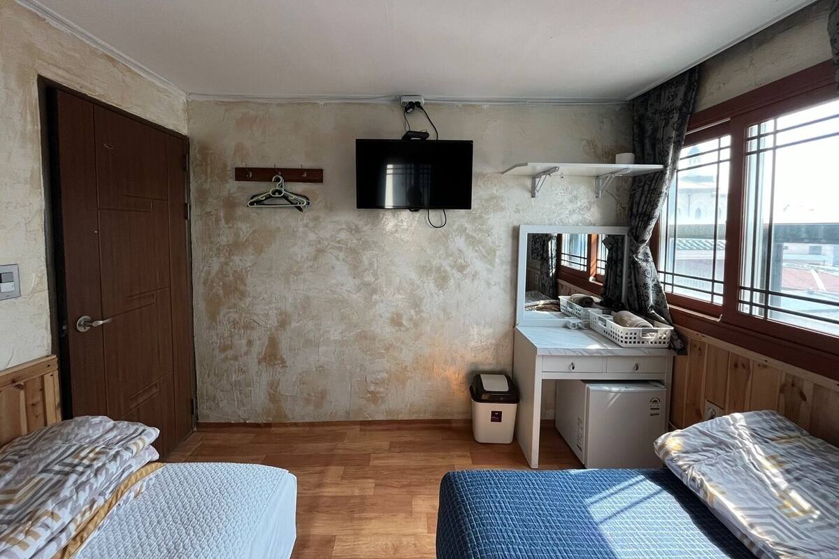 A room with two beds, a desk with a mirror, a television, and a window with curtains.