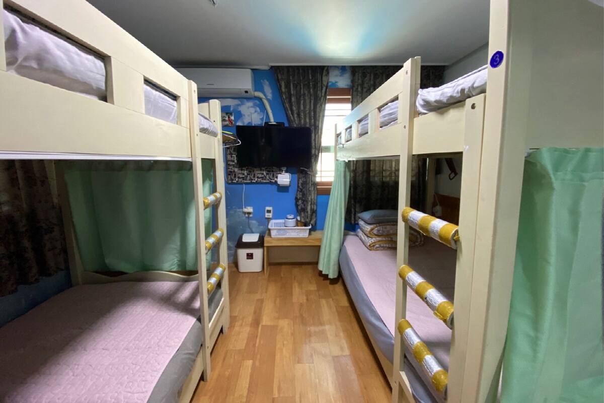 A bunk bed room with a small desk, a television, and a window with curtains.