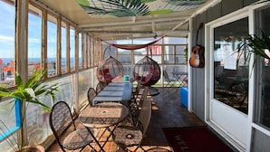 Un espace extérieur abrité, aménagé avec une table et des chaises, de grandes fenêtres et des fauteuils suspendus.