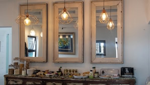 A vintage kitchen with three large mirrors, hanging light fixtures, and a wooden cabinet with drawers. - The Rez Guesthouse (Walvis Bay)