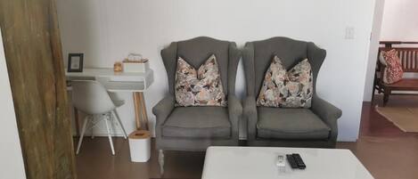 A living room with two grey armchairs, a white coffee table, and a small desk with a chair.