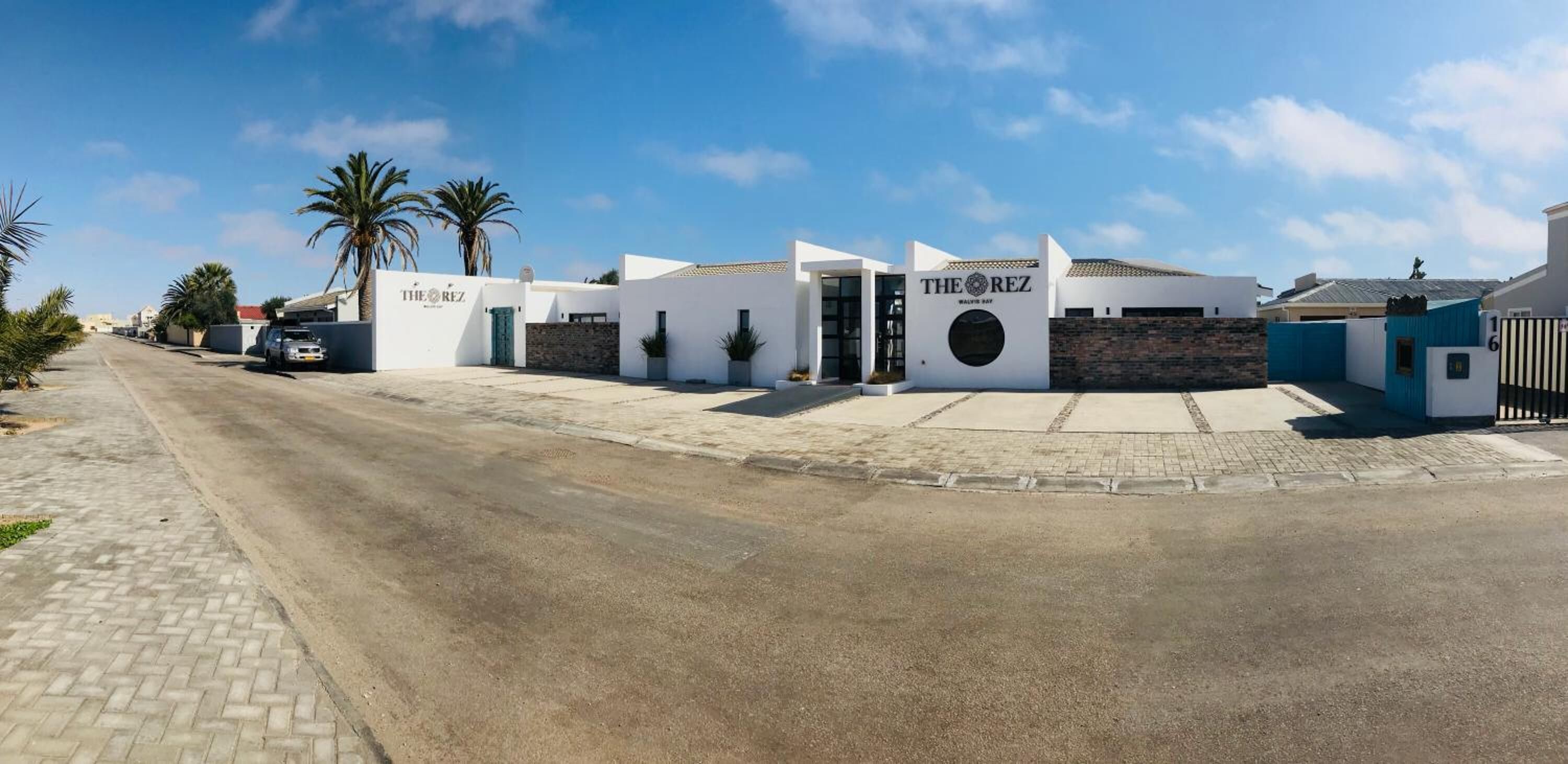 Ein modernes Hotel mit weißer Fassade, einem runden Eingangsbereich und Palmen im Hintergrund.