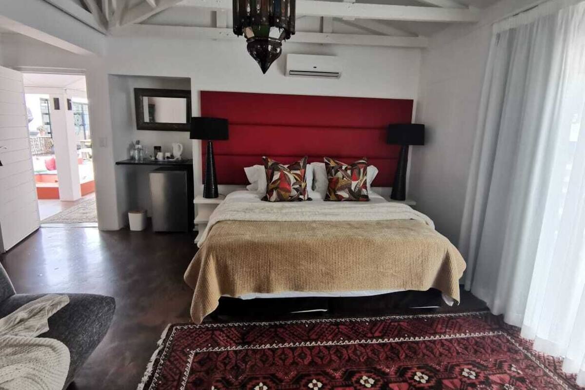 A bedroom with a red headboard, a large bed with patterned pillows, a dark wooden floor, and a red and black patterned rug.