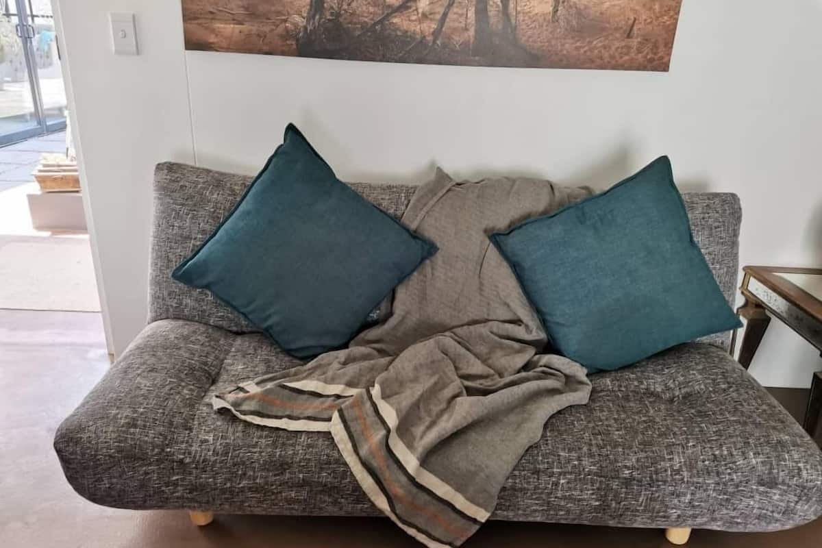 A grey sofa with two teal cushions and a grey blanket.
