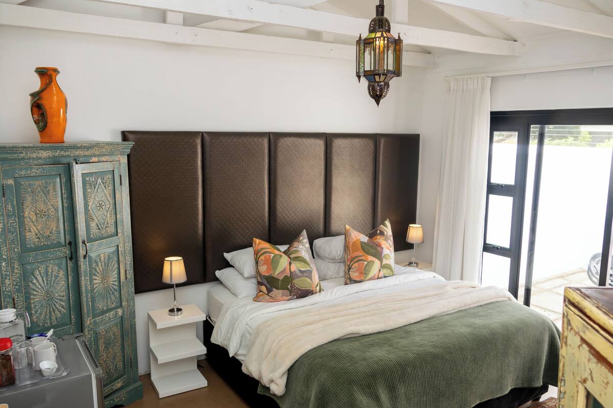A bedroom with a large bed, a nightstand, a lamp, a decorative vase, and a cabinet.