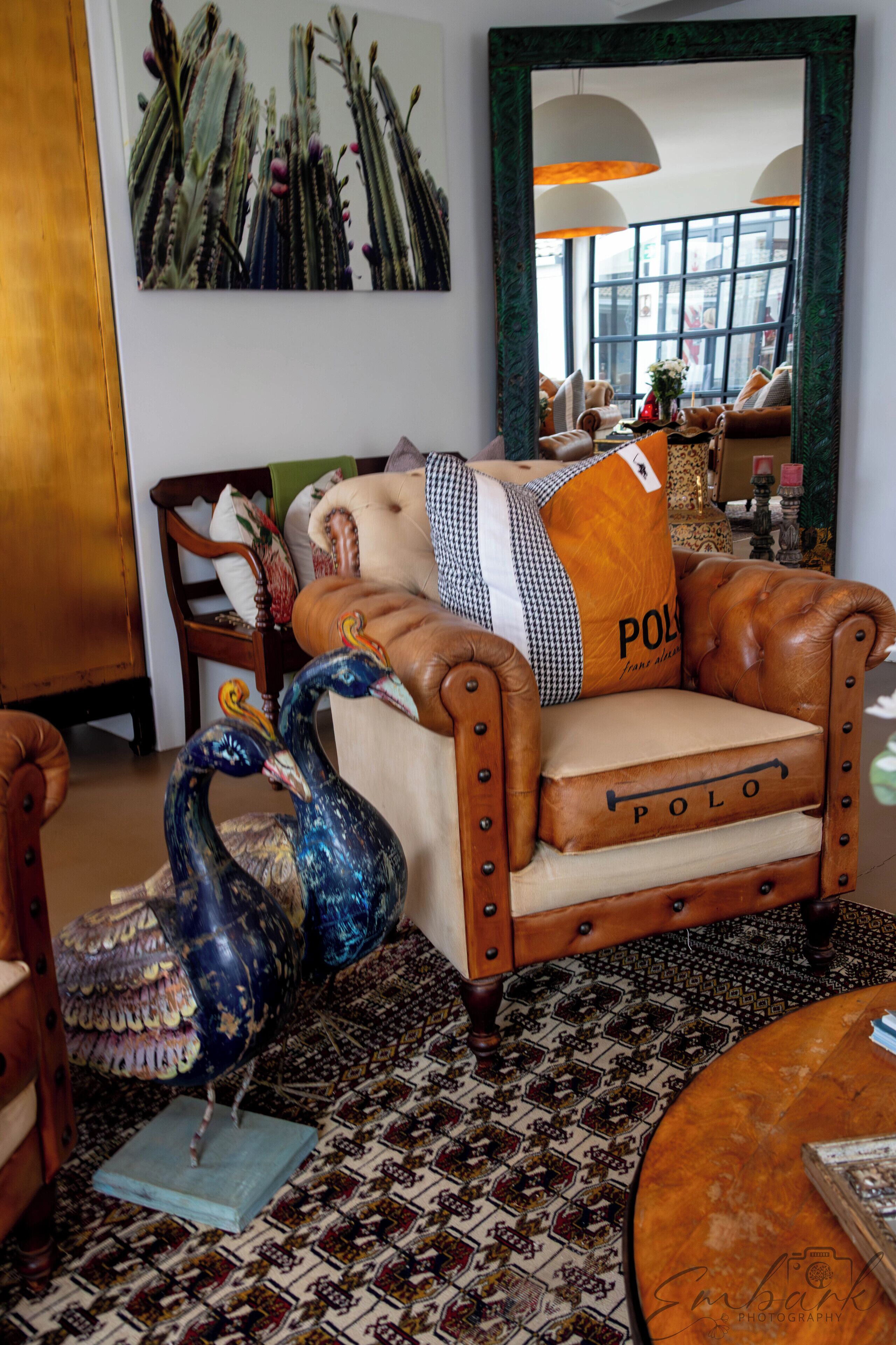 A room with a leather armchair, a peacock sculpture, a patterned rug, and a large mirror reflecting the room.