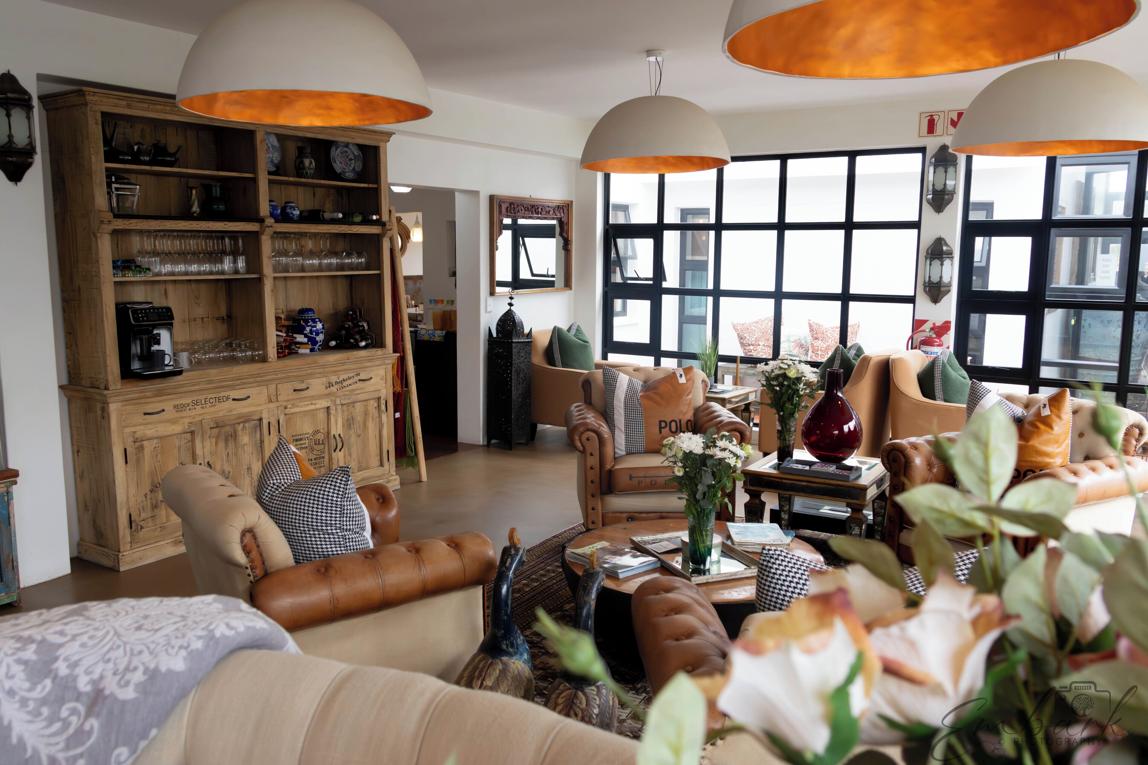 A spacious living room with leather furniture, a wooden cabinet, and large windows providing natural light.