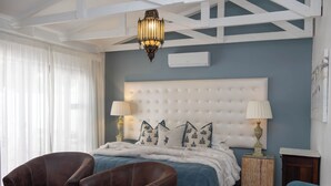 A bedroom with a large bed, two bedside lamps, a chandelier, and a wooden nightstand. - The Rez Guesthouse (Walvis Bay)