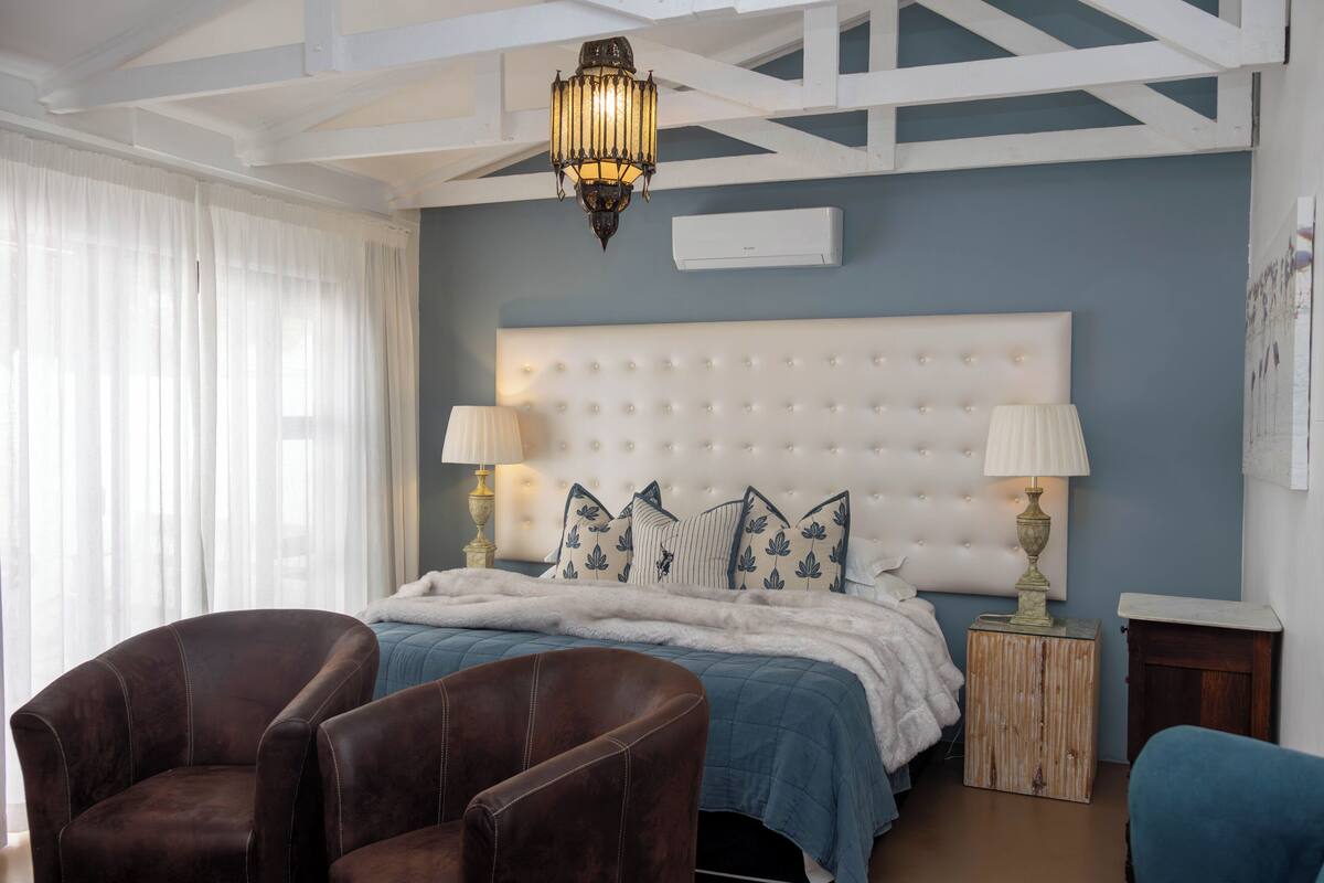 A bedroom with a large bed, two bedside lamps, a chandelier, and a wooden nightstand.