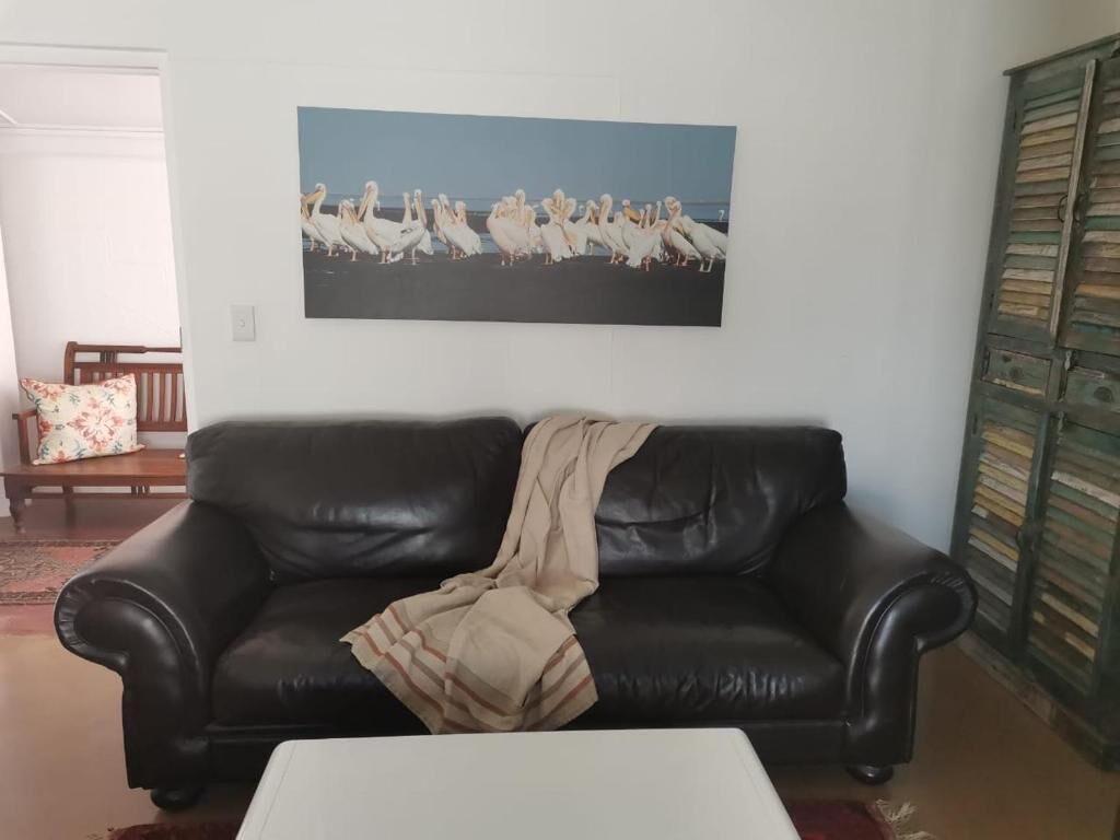 A living room with a black leather sofa, a white coffee table, and a framed picture of birds on the wall.