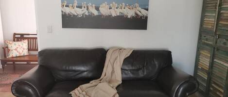A living room with a black leather sofa, a white coffee table, and a framed picture of birds on the wall.