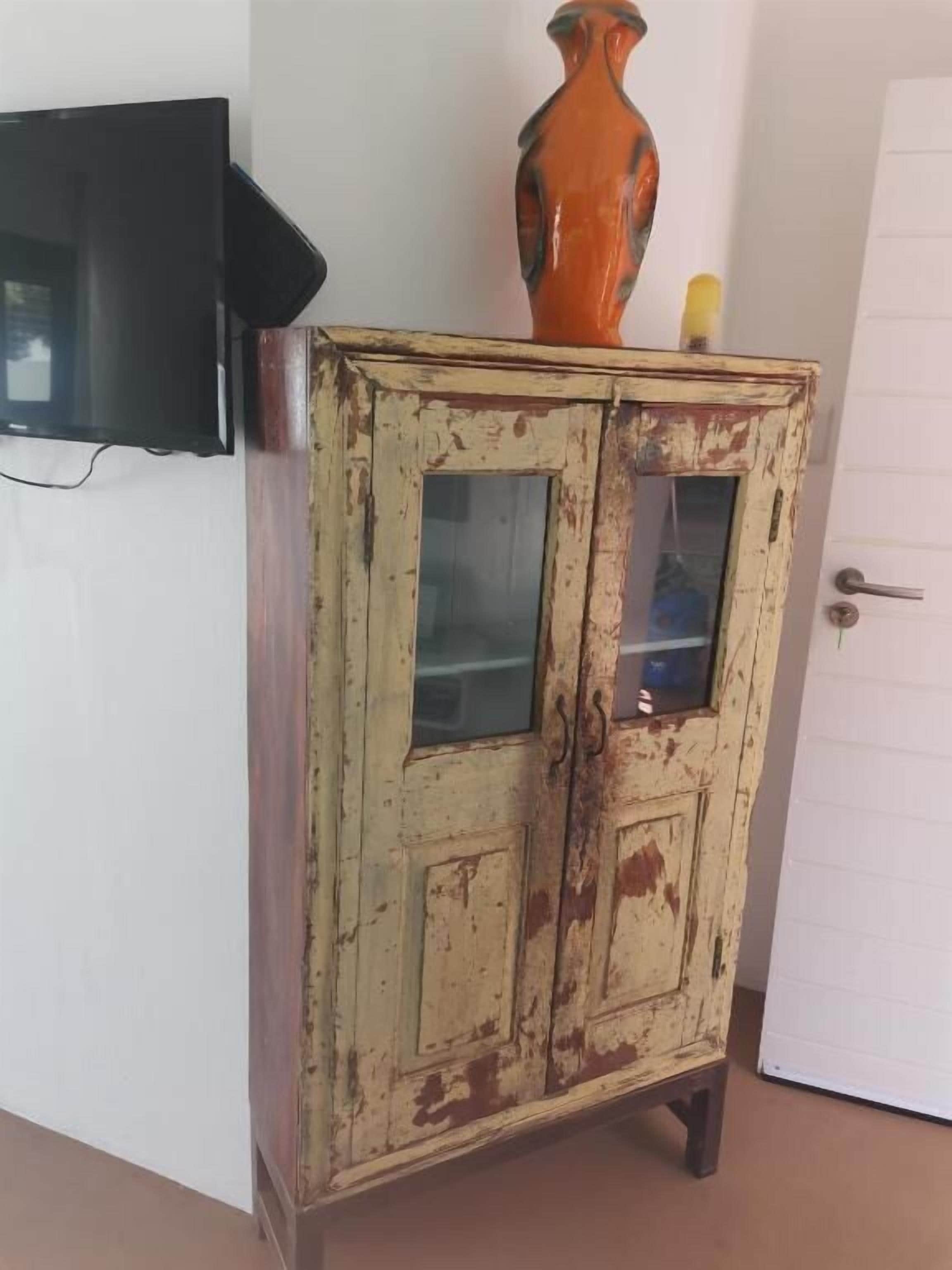 A vintage cabinet with glass doors, a television mounted on the wall, and a vase on top.