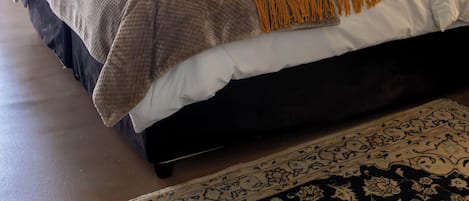 Una cama bien hecha con una manta amarilla, un cabecero oscuro y dos almohadas naranjas.
